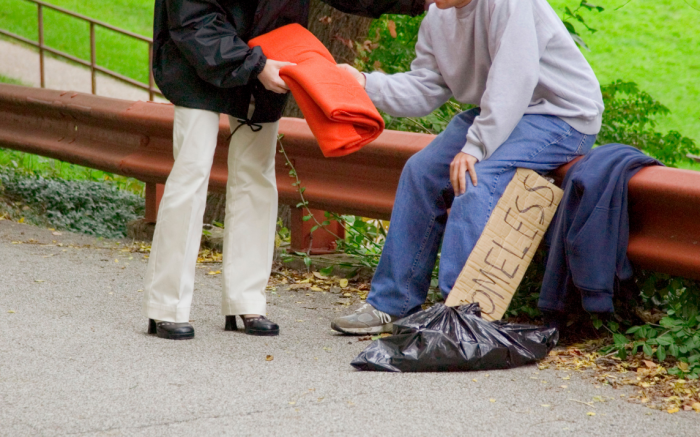 Person handing out blanket to old person with homeless sign