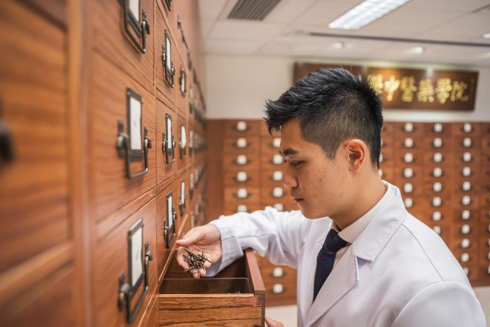 Student wearing medical gown browsing at medicines on shelf