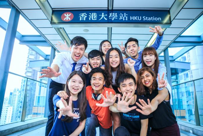 Students smiling under the MTR sign showing the University of Hong Kong