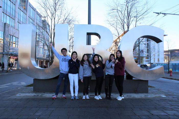 Students smiling in front of University of British Columbia plaque