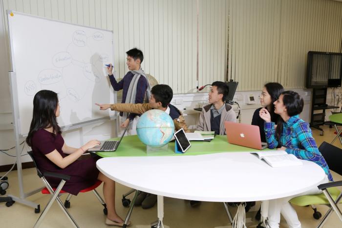 Students working on a whiteboard with laptops and a globe on the desk