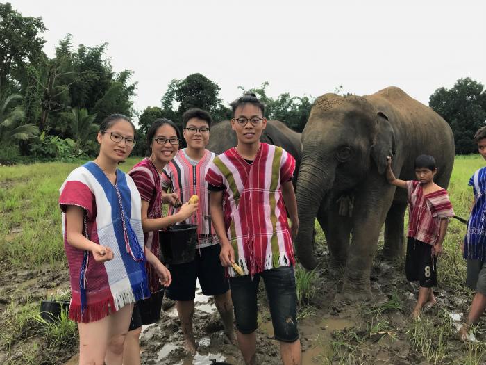 Students wearing traditional outfits smiling in front of an elephant
