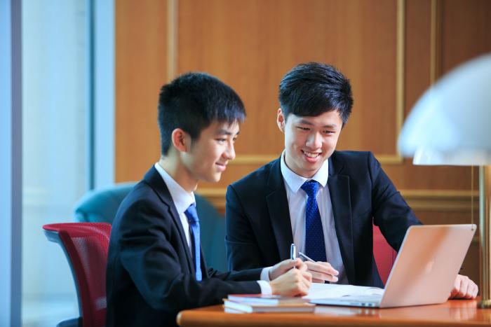 Students in formal attire are looking at a laptop