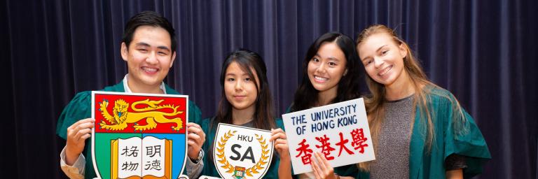 4位身穿綠色長袍的學生大使手持印有香港大學標誌和學生大使標誌的泡沫板