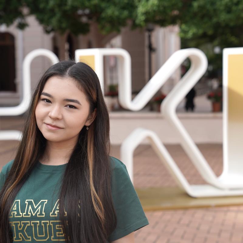 A girl standing with "HKU" sign and smiling